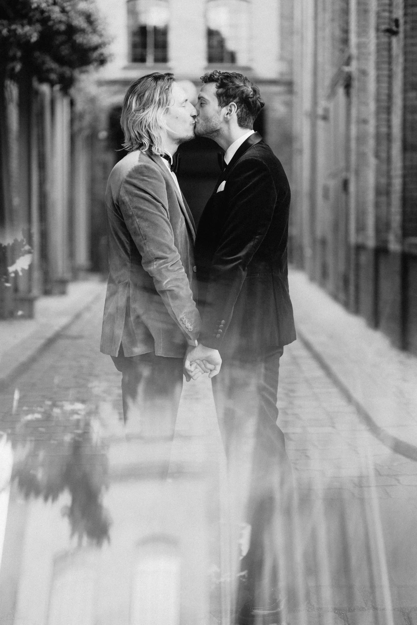 The two grooms kissing on a Berlin street, reflected in the wet pavement